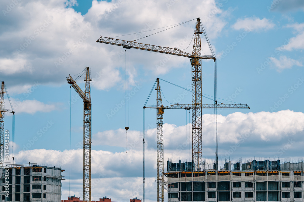 Industrial construction cranes on background of cloudy sky. Hoisting cranes and multi-storey buildings of new city districts. Building site background. Urban area. Industrial construction cranes on background of cloudy sky. Hoisting cranes and multi-storey buildings of new city districts. Building site background. Urban area.