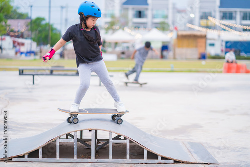Child or kid girl playing surfskate or skateboard in skating rink or sports park at parking to wearing safety helmet elbow pads wrist and knee support