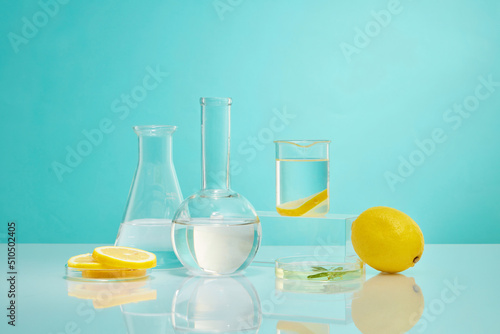 Front view of transparent podium with lemon laboratory equipment and green leaf in blue background science content