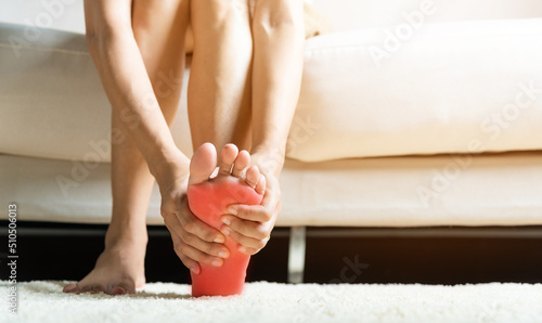 Foot pain, Asian woman sitting on sofa feeling pain in her foot at home, female suffering from feet ache use hand massage relax muscle from soles in home interior, Healthcare and podiatry medical © sorapop