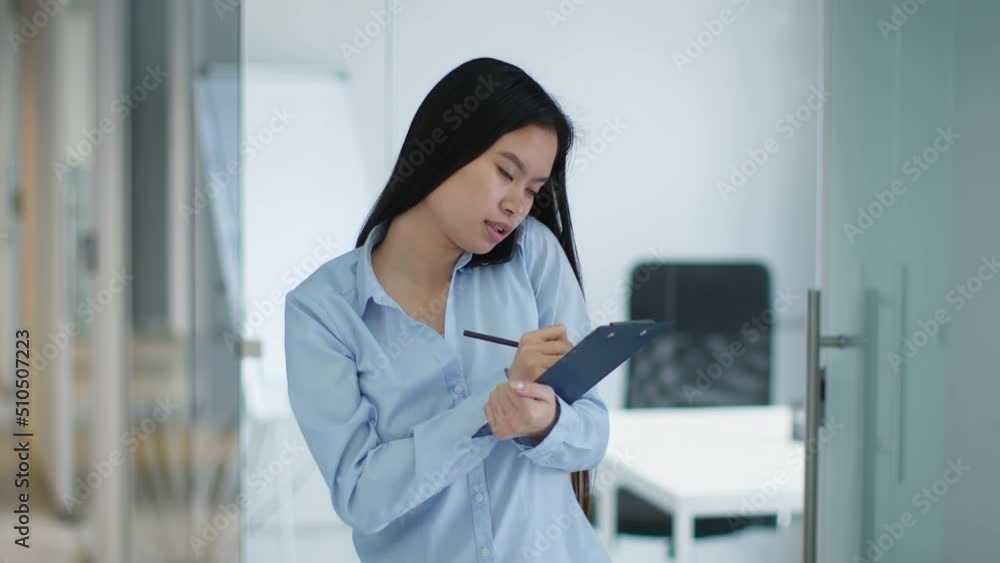 Telemarketing. Young asian woman sales manager talking to client via mobile phone, getting order and writing detail Telemarketing. Young asian woman sales manager talking to client via mobile phone, getting order and writing detail