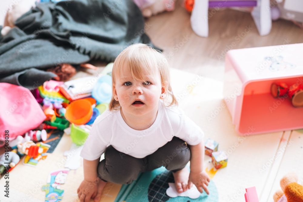 Cute funny baby girl sitting on floor in children room at home Cute funny baby girl sitting on floor in children room at home
