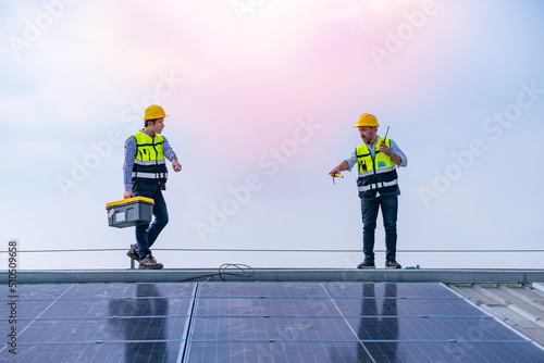 Engineers walking on roof inspect and check solar cell panel by hold equipment box and radio communication ,solar cell is smart grid ecology energy sunlight alternative power factory concept.