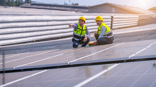 Engineers walking on roof inspect and check solar cell panel by hold equipment box and radio communication ,solar cell is smart grid ecology energy sunlight alternative power factory concept.