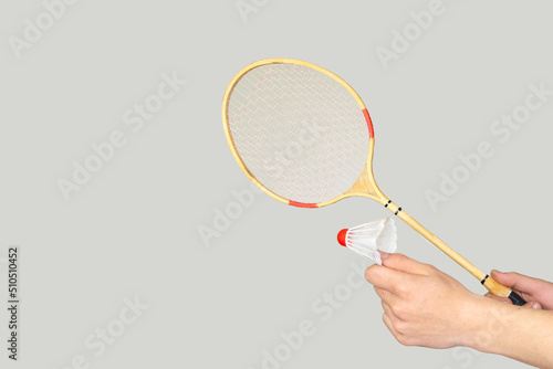 man's hand holding a badminton racket on grey background.