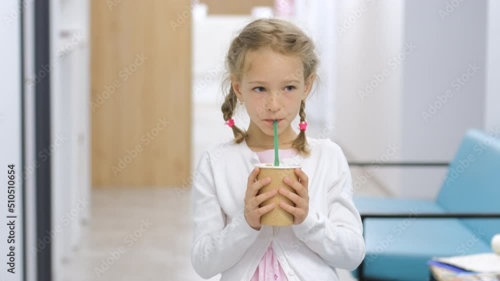 Cute caucasian little girl holding cardboard cup and drinking hot chocolate from a straw indoors Cute caucasian little girl holding cardboard cup and drinking hot chocolate from a straw indoors