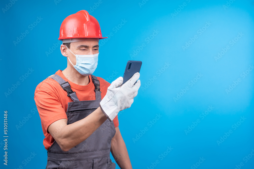 Male builder in face mask using smartphone during work Male builder in face mask using smartphone during work
