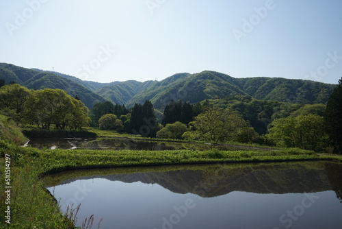 日本の青鬼集落。周囲を山に囲まれた場所で、田んぼや畑が広がる風景。田植えが始まる時期、朝の光で水鏡が美しい。