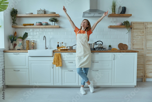 Fotografiet Full length of beautiful young woman looking happy while standing at the domesti