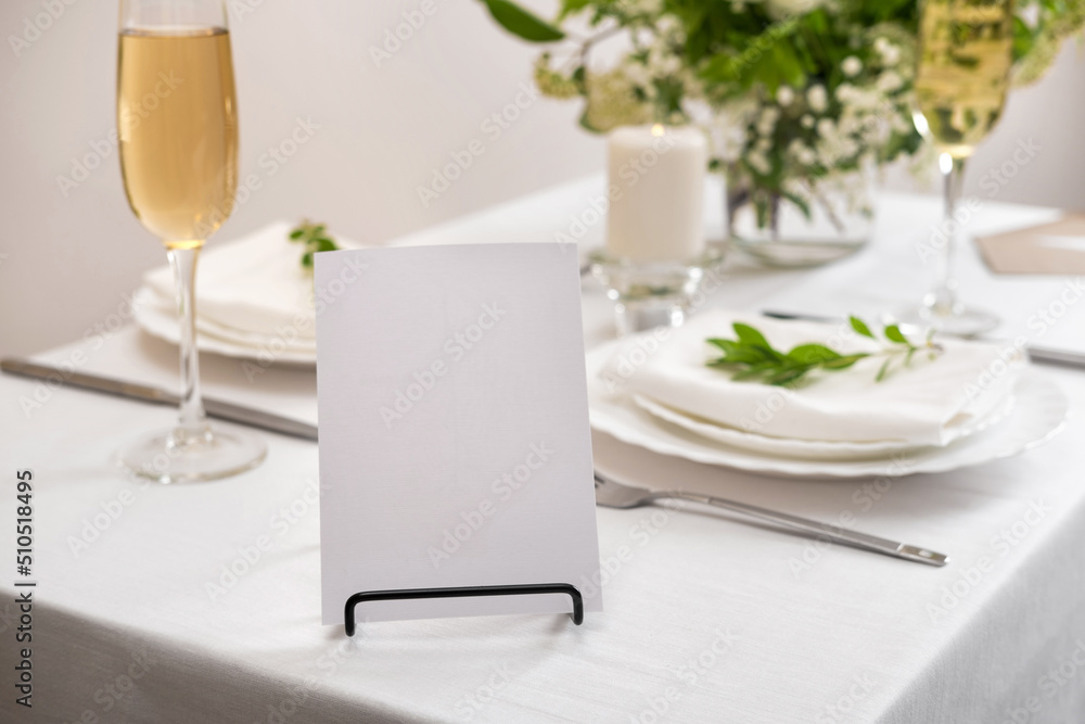 Mockup white blank space card for table number or menu. Wedding teble decoration with white flowers, glasses and white napkins. Elegantly decorated table at a wedding reception. 