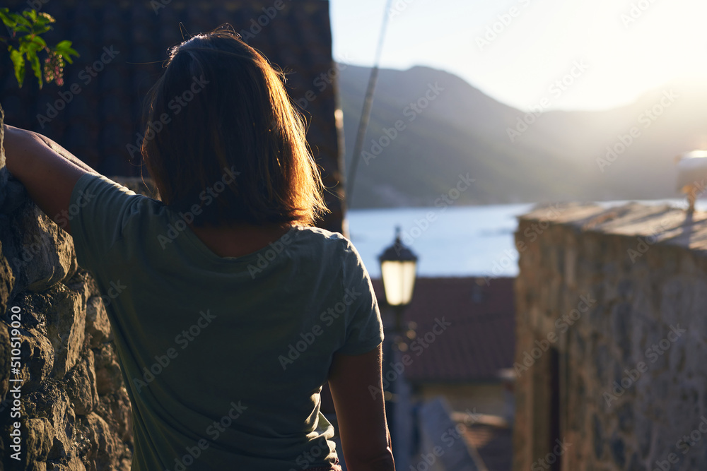Woman in summer vacation. Young woman enjoy sunset on balcony in small old town on seaside in Montenegro looking at view on sea. Woman in summer vacation. Young woman enjoy sunset on balcony in small old town on seaside in Montenegro looking at view on sea.