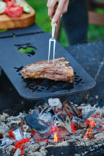 Turning beef steak with fork on barbecue grid