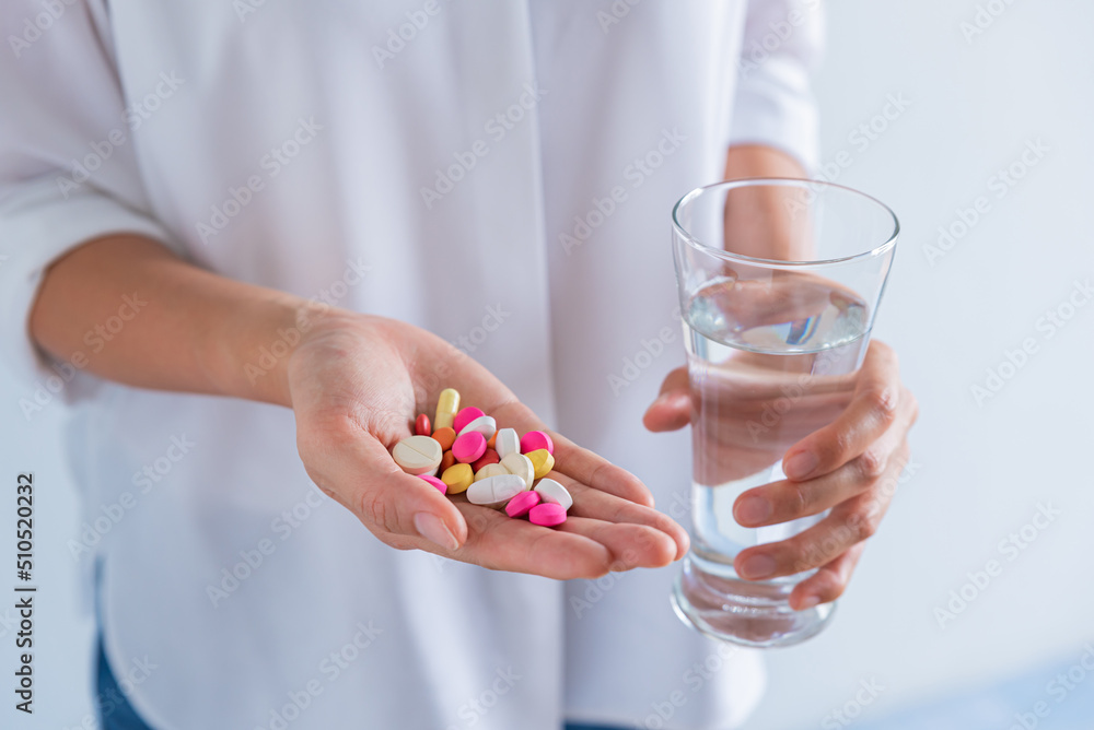 woman hand holding many pills and a glass of water woman hand holding many pills and a glass of water