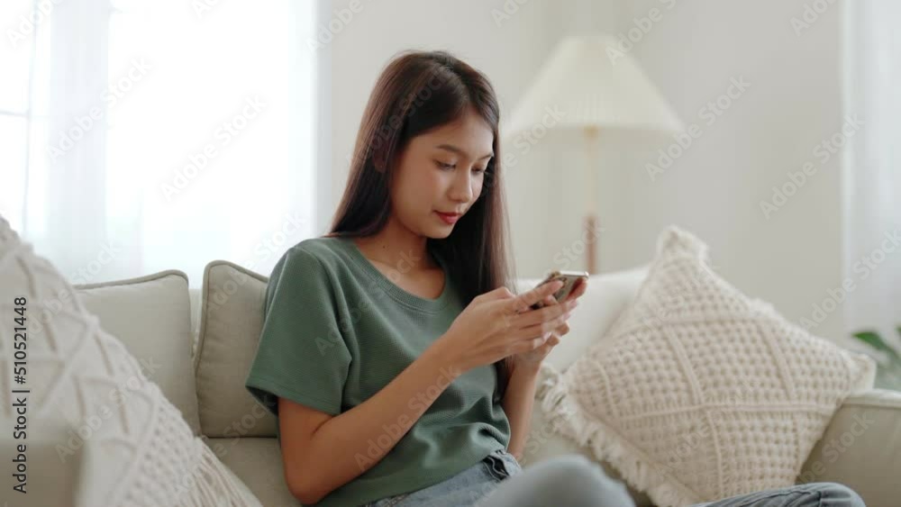 Happy young asian woman relax on comfortable couch at home texting messaging on smartphone, smiling girl use cellphone chatting, browse wireless internet on gadget, shopping online from home Happy young asian woman relax on comfortable couch at home texting messaging on smartphone, smiling girl use cellphone chatting, browse wireless internet on gadget, shopping online from home