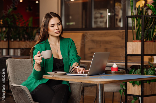 Female blogger or freelancer drinking coffee and working with a laptop in the cafe or coworking area