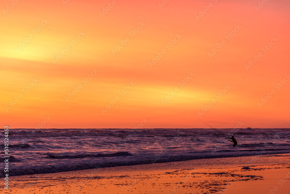 Fisherman silhouette from the shore with his rod at the seashore at sunset 