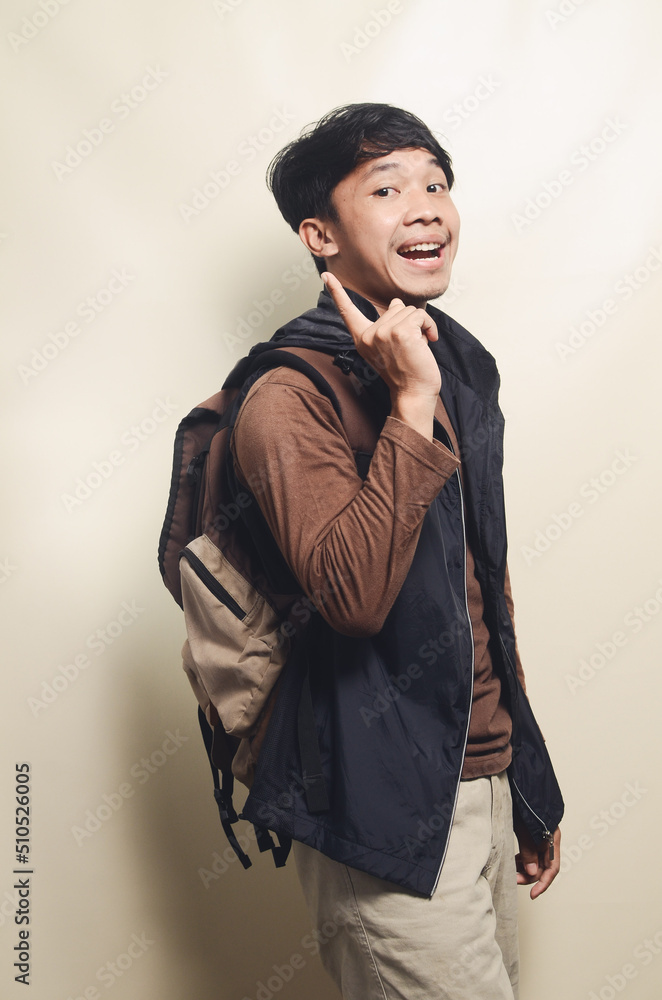 Portrait of Asian college young man pointing at empty space wearing brown t-shirt and black vest Portrait of Asian college young man pointing at empty space wearing brown t-shirt and black vest
