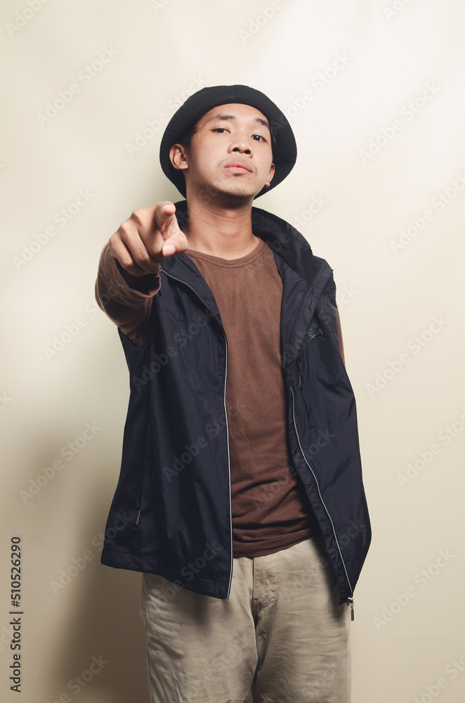portrait of asian young man greeting his friend wearing hat, brown t-shirt and black vest isolated on background portrait of asian young man greeting his friend wearing hat, brown t-shirt and black vest isolated on background