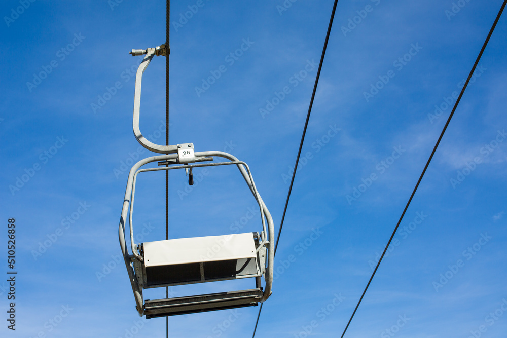 View on a single, hanging chairlift. Blue sky in the background, no people. View on a single, hanging chairlift. Blue sky in the background, no people.