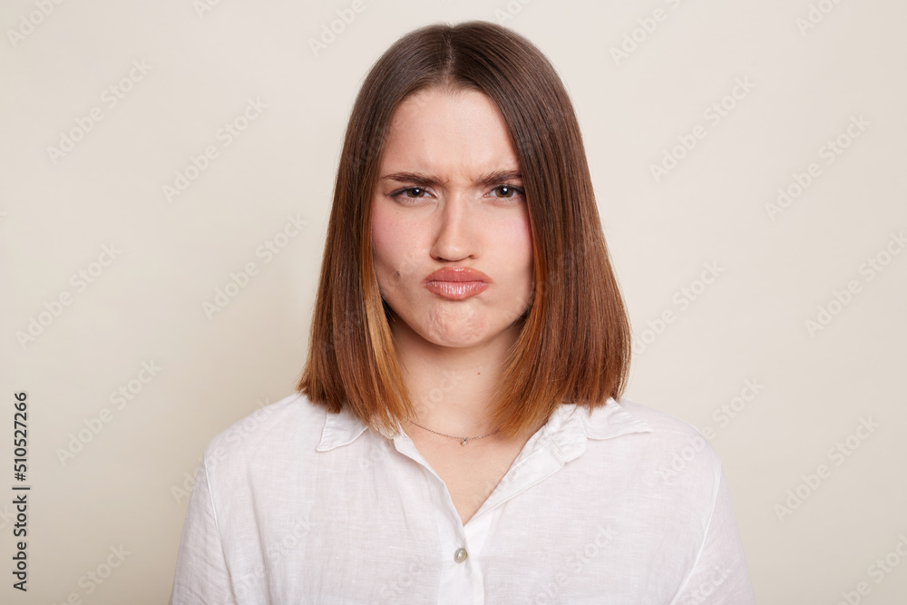 Image of Caucasian dark haired attractive woman wearing shirt, looking at camera with pout lips, being sad and confused, posing isolated over white background. Image of Caucasian dark haired attractive woman wearing shirt, looking at camera with pout lips, being sad and confused, posing isolated over white background.