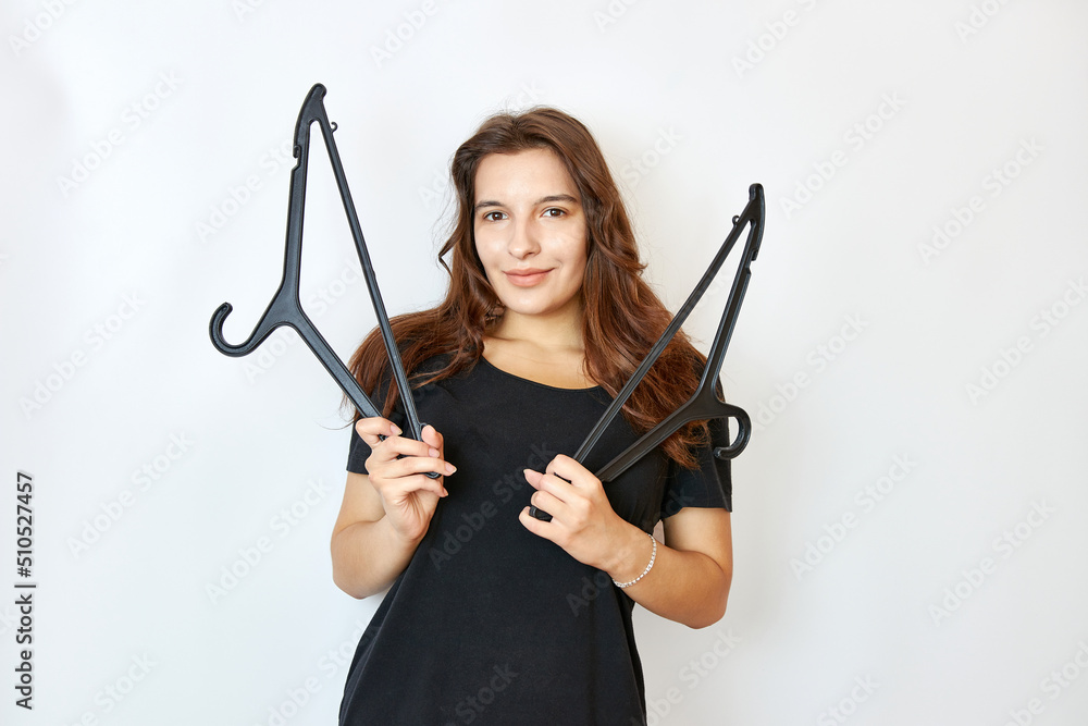 Beautiful girl in a black T-shirt holding two hangers. The concept of buying clothes. Beautiful girl in a black T-shirt holding two hangers. The concept of buying clothes.