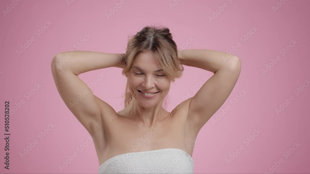 Studio portrait of happy middle aged lady making ponytail, doing hairstyle herself, smiling to camera, pink background Studio portrait of happy middle aged lady making ponytail, doing hairstyle herself, smiling to camera, pink background