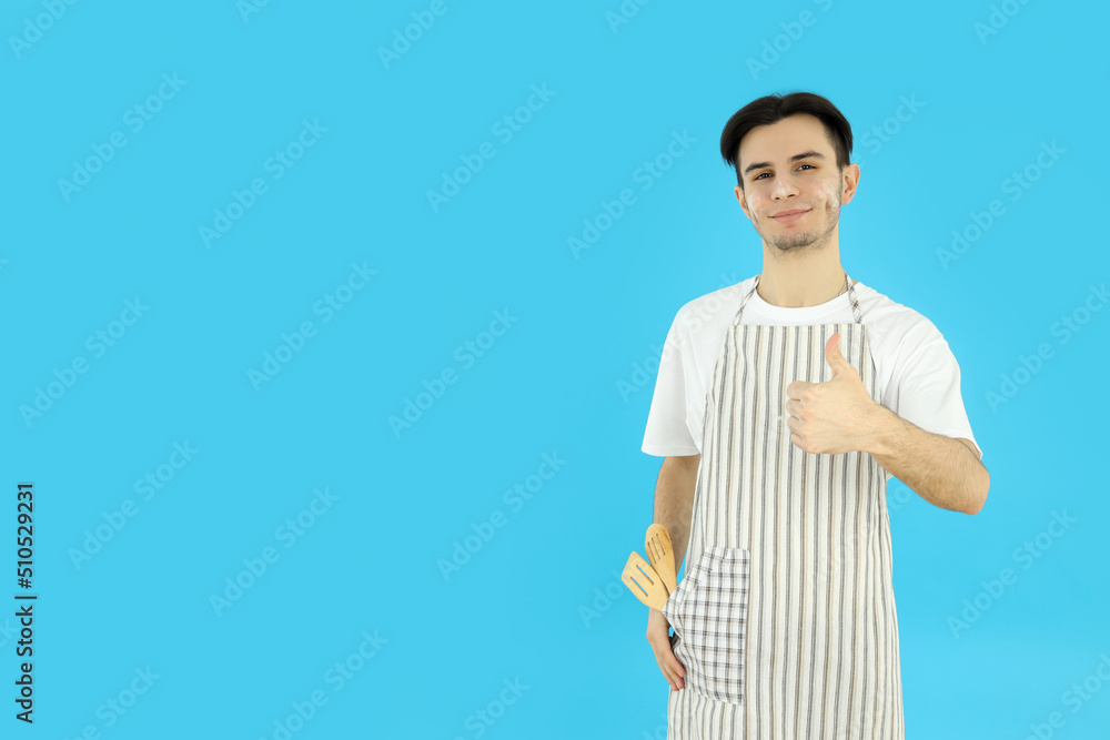 Concept of cooking, young man in apron on blue background Concept of cooking, young man in apron on blue background