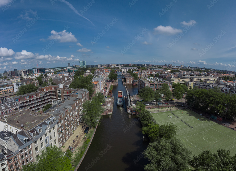 Aerial drone panoramic view of a ship passing elevating road bridge in amsterdam canal. Ship under open bridge over the canal.