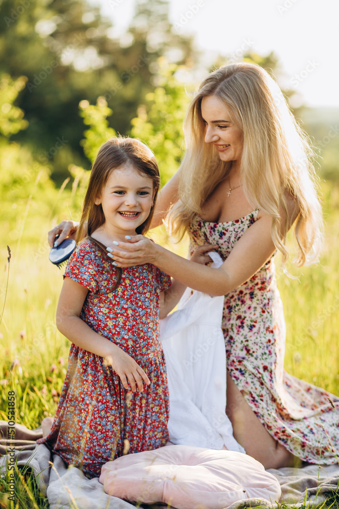 mom combs her daughter's hair in nature. Woman with two daughters sitting in the Park
