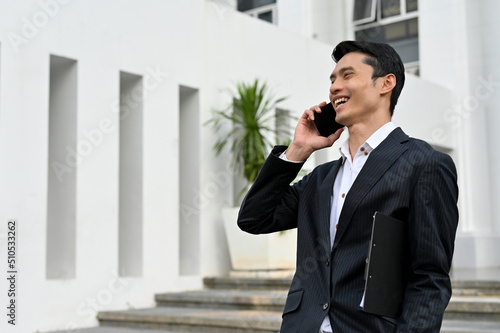 Asian businessman in formal suit, standing outside of the building and talking on the phone