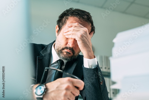 Overworked businessman at office desk, tired fatigued business owner in stressful situation