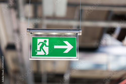 Illuminated emergency exit sign, hanging from the ceiling. With running figure and an arrow which points to the right.