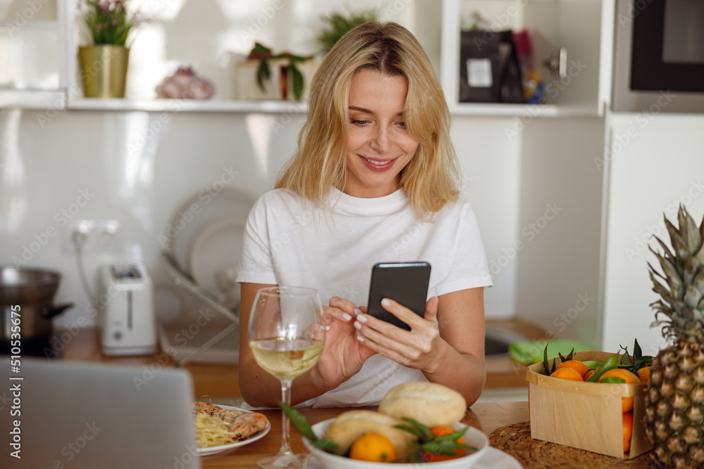 Caucasian pretty woman holding smartphone and scrolling or texting. Having lunch at home.