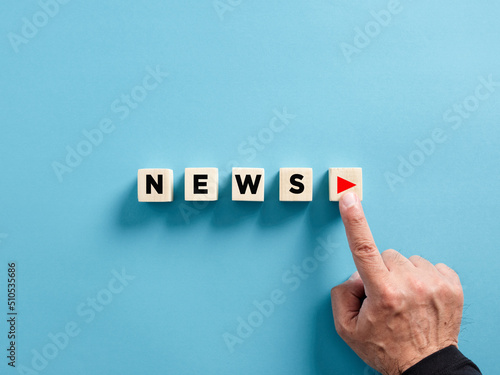 Male hand presses the play button with the news on wooden cubes. Broadcasting, publishing or watching the latest news