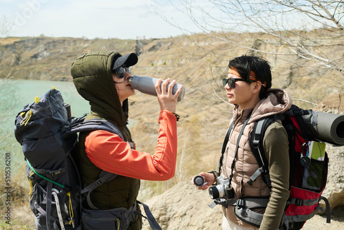 Side view of young Asian women hiking around quarry on spring day drinking tea or water from vacuum flask