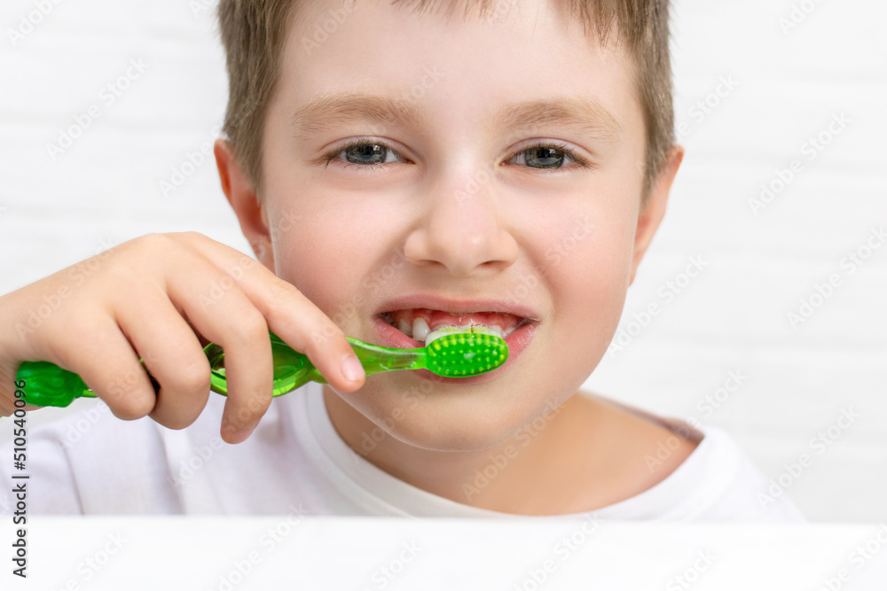 Portrait of cute smiling boy holds a toothbrush and cleans his teeth at home. Child looking at camera. Kid brush a milk tooth. Dental care and morning daily routine for childrens health. Portrait of cute smiling boy holds a toothbrush and cleans his teeth at home. Child looking at camera. Kid brush a milk tooth. Dental care and morning daily routine for childrens health.