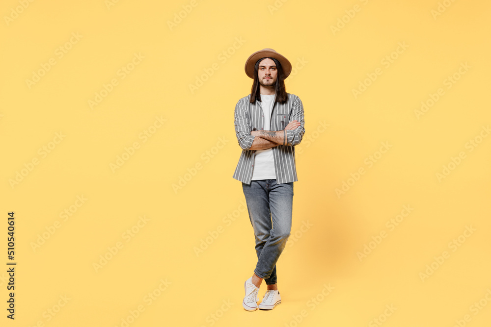 Fototapeta premium Full body young smiling man he 20s wears striped grey shirt white t-shirt hat look camera hold hands crossed folded isolated on plain yellow color background studio portrait. People lifestyle concept.
