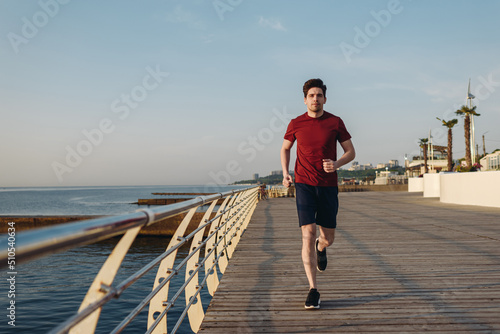 Fototapeta Naklejka Na Ścianę i Meble -  Fulll body young strong sporty athletic toned fit sportsman man 20s wear sports clothes warm up jogging run training at sunrise sun dawn over sea beach outdoor on pier seaside in summer day morning.