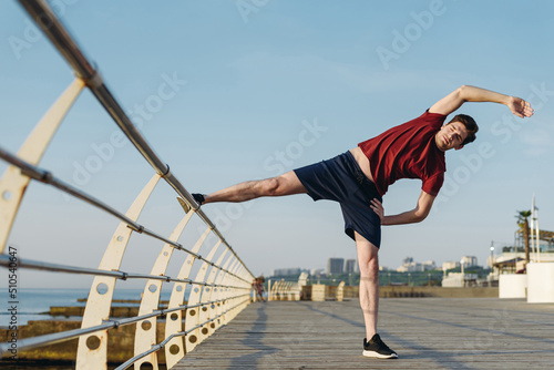 Full body young strong sporty fit sportsman man 20s wear sports clothes warm up train do stretch lunge exercise rising hands up at sunrise sun dawn over sea beach outdoor on pier seaside in morning. © ViDi Studio