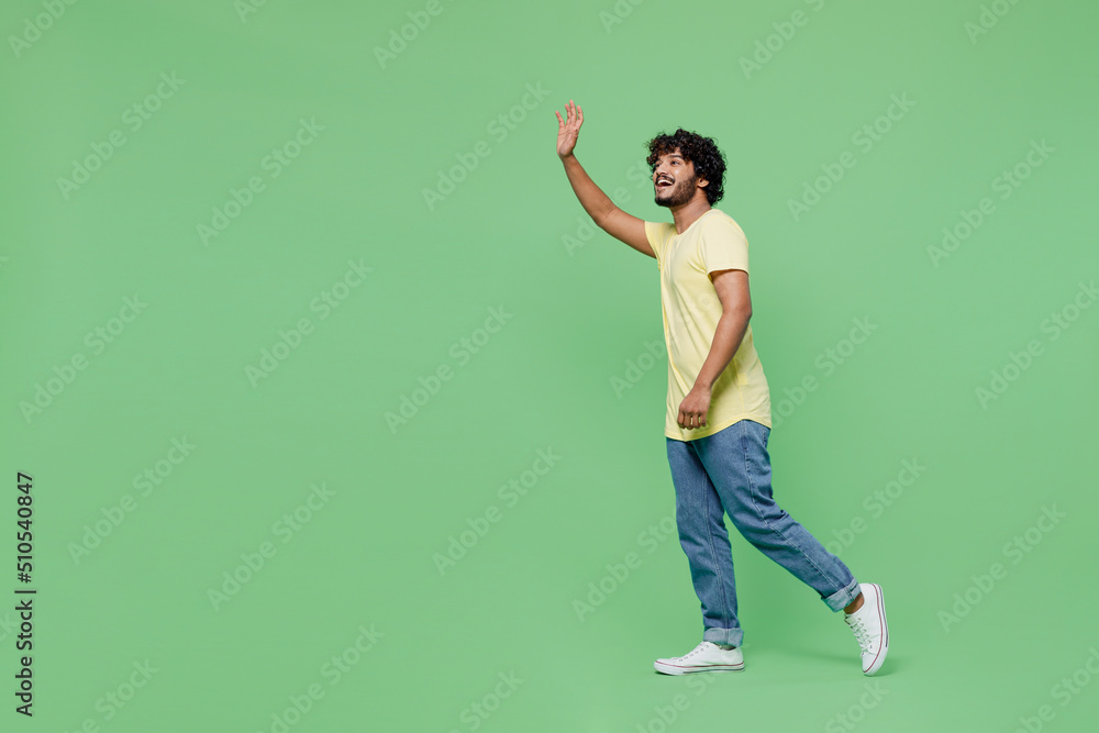 Full body young smiling happy Indian man 20s wearing basic yellow t-shirt walk going strolling waving hand isolated on plain pastel light green background studio portrait. People lifestyle concept Full body young smiling happy Indian man 20s wearing basic yellow t-shirt walk going strolling waving hand isolated on plain pastel light green background studio portrait. People lifestyle concept