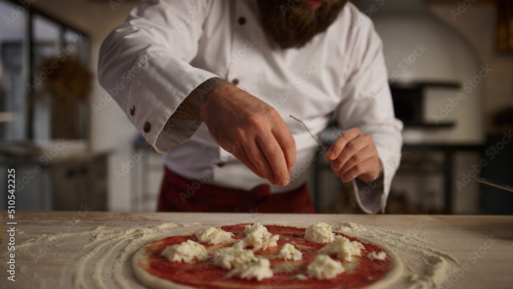 Kitchen chef cooking pizza in professional restaurant. Man adding spice on food.