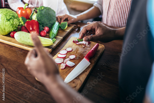 Close up shoot of black man holding sharp knife cutting vegetables on wooden board, making fresh salad using organic ingredients.