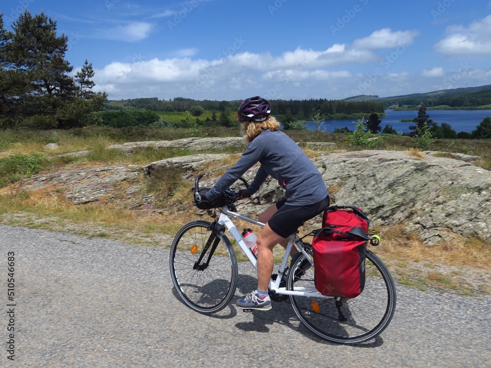 Fototapeta premium Jeune femme à vélo et bicyclette avec sacoche en cyclotourisme sur les pistes cyclables et voies vertes du sud de la France région Occitanie montagne Noire Lacaune Espinouse 