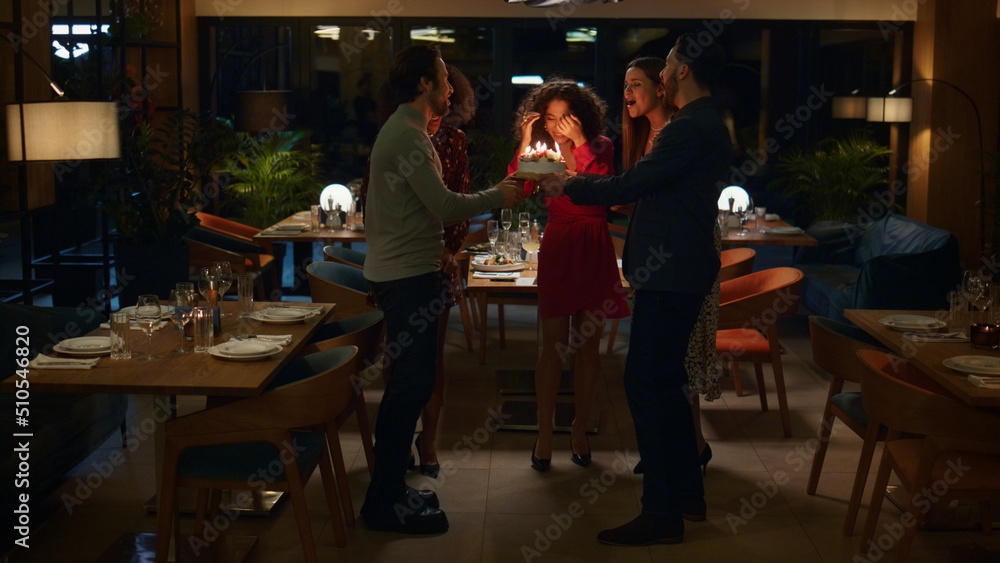 Naklejka premium Surprised woman blowing cake on birthday party. Friends celebrate in restaurant.