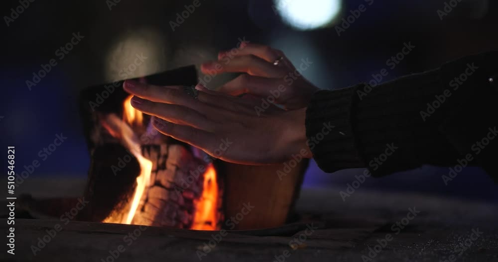 Close-up of burning logs in the fire of a street cafe in winter. An unrecognizable woman, warming her hands Close-up of burning logs in the fire of a street cafe in winter. An unrecognizable woman, warming her hands