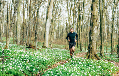 wide shot of sporty man running in beautiful spring forest. Sport and wellness concept