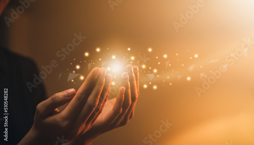 Hand praying with magic light that flows through on orange bokeh background.