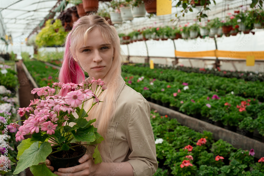 Salesperson of garden mall holding blossoming plant in pot in hands standing in greenhouse
