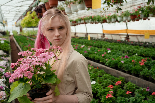 Salesperson of garden mall holding blossoming plant in pot in hands standing in greenhouse © Natalia Navodnaia