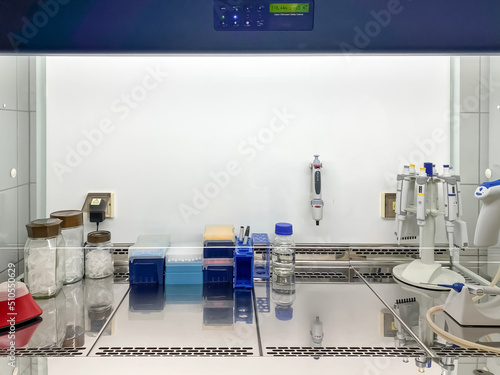 Laboratory equipment used in cell culture (pipette tips with filter, microcentrifuge tubes,  vortex, tube racks, bottle with ethanol, glass beaker, etc.) placed under the laminar flow chamber.